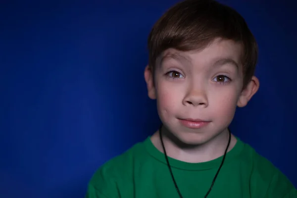 Portret van een geschokte negen jaar oude blonde jongen op een blauwe achtergrond — Stockfoto