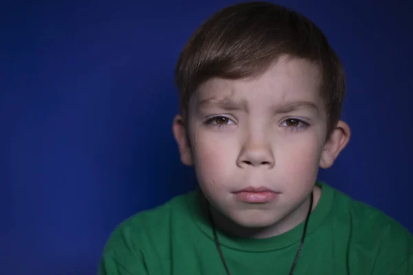 Retrato de um triste menino loiro de nove anos pensivo em um fundo azul — Fotografia de Stock