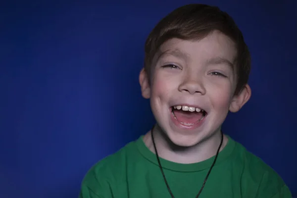 Portrait d'un garçon blond heureux et paisible de neuf ans souriant sur un fond bleu — Photo