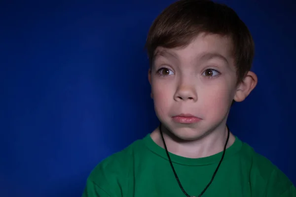 Portrét šokovaného devítiletého blonďatého chlapce na modrém pozadí — Stock fotografie