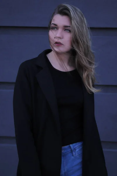 Stadtporträt einer nachdenklichen, flirtenden schönen Frau in schwarzer Bluse und Jeans auf grauem Wandhintergrund in Streifen — Stockfoto