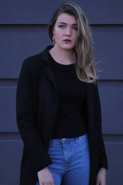 Retrato urbano de una hermosa mujer coqueta pensativa en blusa negra y jeans sobre un fondo de pared gris en tiras —  Fotos de Stock