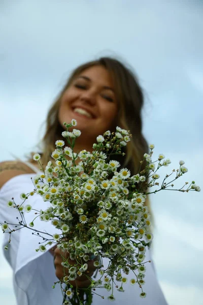 Retrato de una mujer hermosa coqueta feliz en blusa blanca en el campo. Llevando un ramo de margaritas. Tatuaje temporal. Dibujos en el cuerpo. hippie. Naturaleza amorosa . — Foto de Stock