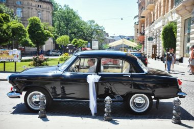 Lviv, Ukraine - June 5, 2011: Soviet car 60-xx years Volga GAZ-21. The driver expects young couple is crowned in the church clipart