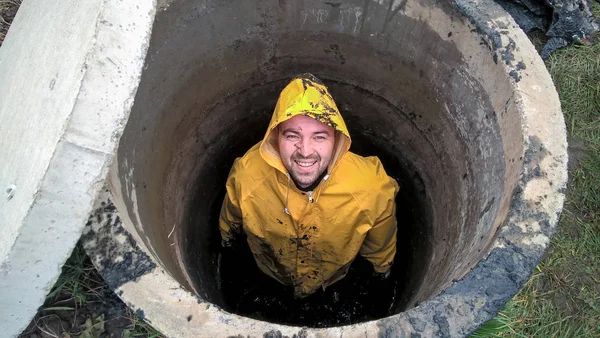 O homem está dentro do poço de esgoto, obras de esgoto, trabalho perto de casa — Fotografia de Stock