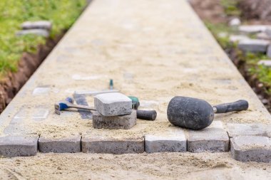 Process of laying pavement at yard. Stones are laying on sand. Work tools. clipart