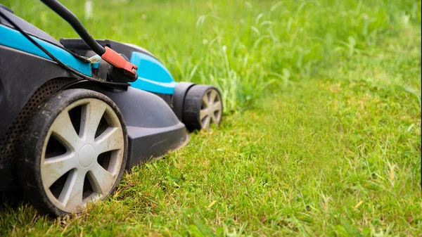 Bahçedeki çimlerin üzerinde elektrikli çim biçme makinesi. Bahçe ve çim bakımı teması. Kopyalama alanı olan sancak biçimi