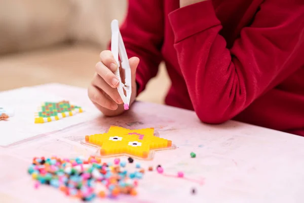 Küçük kız elinde boncukla bir cımbız tutuyor. Füzyonlu renkli boncuklardan sanat oyuncağı yapıyor. Son dokunuşlar. Perler boncukları olarak da bilinir. Çocukların hayal gücünü geliştiren oyuncaklar. Süreç kapanıyor