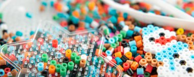 Bir dizi boncuk. Perler tahtası, cımbız ve bir sürü renkli füzyon boncuğu. Çocukların hayal gücünü geliştiren oyuncaklar. Çocuk oyuncakları teması. Geniş arkaplan boşluğu