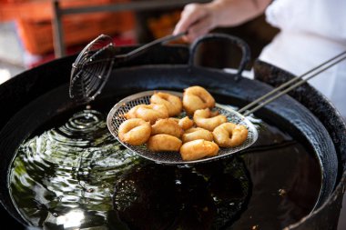 Aşçı elek üzerinde taze pişmiş donut servis ediyor, yağdan yeni alınmış. Açık hava festivalinde nefis fast food.