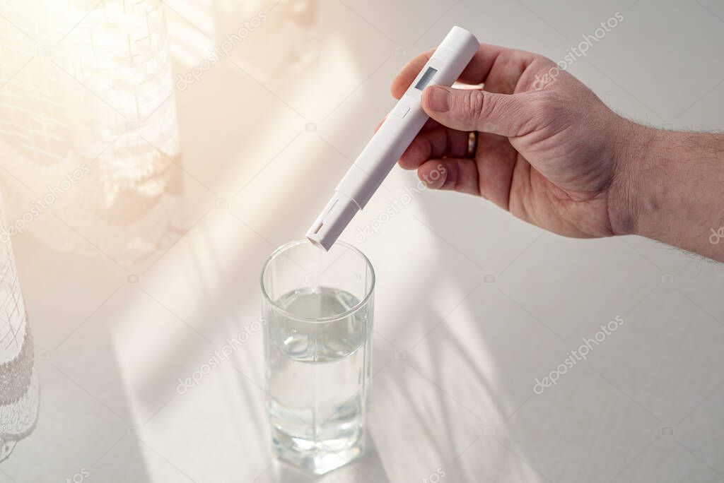Man going to check level of water purity using a portable water TDS meter tool, close up. Before test a device shows 0 ppm of contaminant level. Process takes place at home in the kitchen.