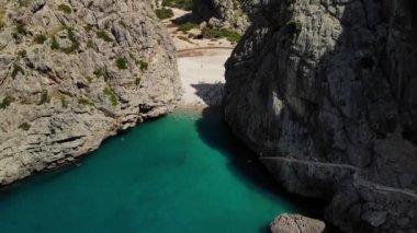 İnsanlar yüksek kayalık dağlar arasındaki plajda dinleniyor. Sa Calobra köyü, Majorca Adası 'nda popüler bir turizm beldesidir. Hava aracı görüntüsü, 4K