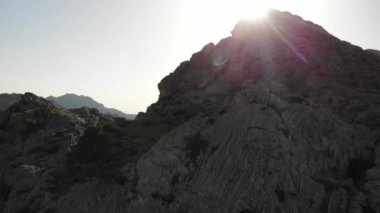 Kayalık dağın tepesinin hava aracı görüntüsü güneş ışığıyla aydınlatılıyor. Güneş ışınları ve güneş ışığı sahneyi daha da güzelleştiriyor. Dağlık arazi, yürüyüş yapmak ve manzaranın tadını çıkarmak için güzel bir yerdir.