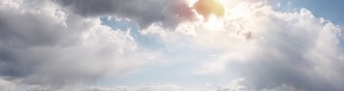 Sıcak, güneşli tonları olan bulutlu güzel bir manzara. Mavi gökyüzü bulutlarla kaplı. Sıcak güneş ışığı ve güneş ışınları bulutların arasından geçer ve onları aydınlatır. Ultra geniş panoramik doğal arkaplan.