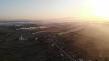Kuru otlar tarlalarda yanıyor. Köy duman altında. Sonbaharın başında. Hasat zamanı. Geleneksel Ukrayna köyünün üzerinde, günbatımı saatinde hava üstgeçidi. Köyler ve kırsal bölgelerle ilgili görüntülerin toplanması