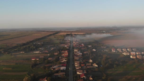 ドローンは村の上空を飛ぶ 道路に沿って小屋 煙は畑から広がっている 日没時間 — ストック動画