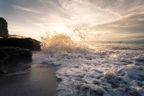 Onda oceânica com espuma batendo contra as rochas ao pôr do sol — Fotografia de Stock