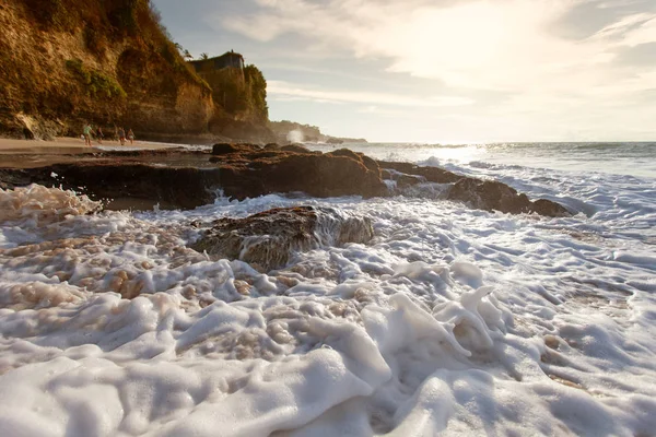 Onda oceânica com espuma batendo contra as rochas ao pôr do sol — Fotografia de Stock