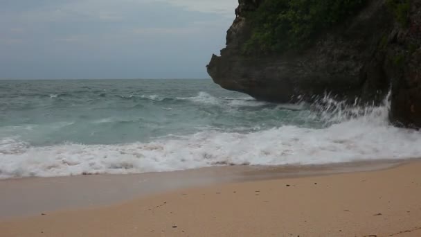 Морская волна ударила по скалам на песчаном пляже — стоковое видео