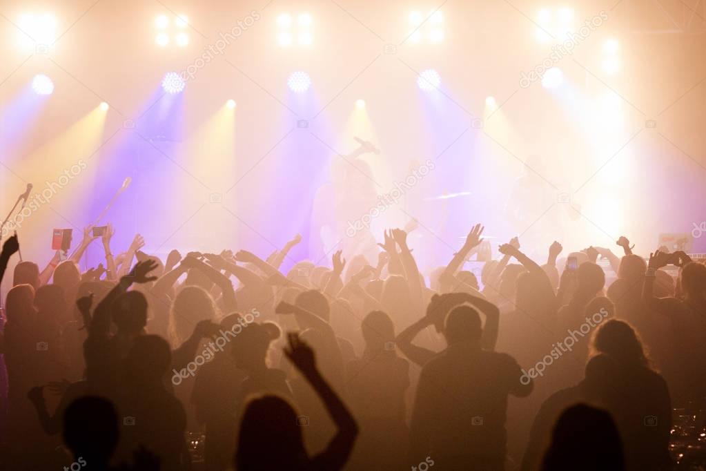 The audience at a concert with arms raised in silhouette