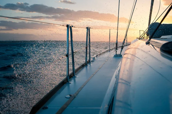 Вітрильна яхта на заході сонця, хвилі і бризки — стокове фото