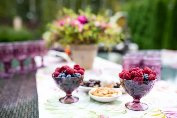 Gyönyörű szemüveg színes lila üveg az asztalon bogyókkal és virágokkal — Stock Fotó