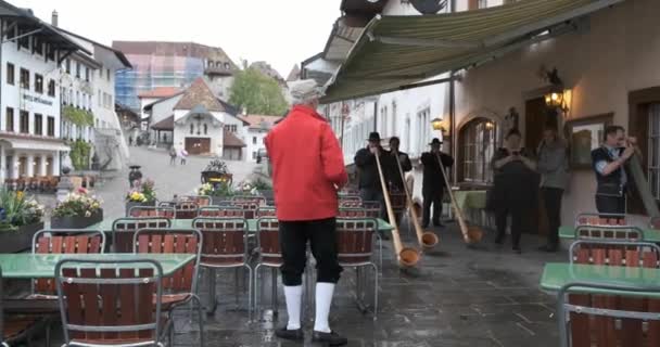 Груйер, Швейцария - 2 мая 2019 года: местные музыканты в традиционной одежде исполняют музыку под колокола на городской площади — стоковое видео