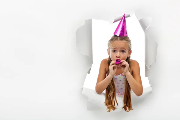 Surprise - little girl with party horn popping out from a torn p — Stock Photo, Image