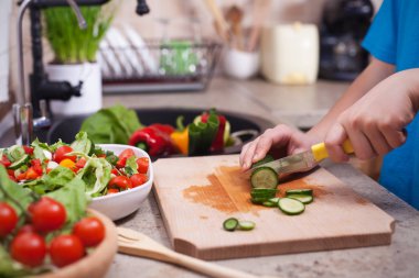 Çocuk elinde bir salatalık bir salata için dilimleme