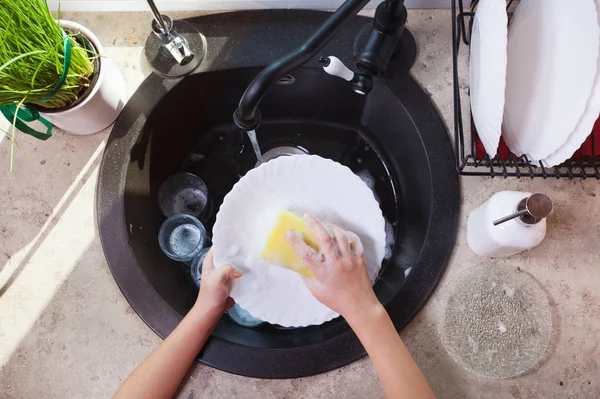 Manos de niño fregando un plato con esponja en el fregadero de la cocina —  Fotos de Stock