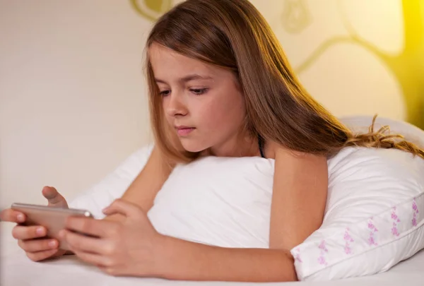 Menina usando smartphone deitado na cama, profundidade rasa — Fotografia de Stock