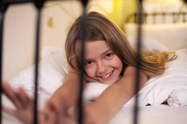 Молодая девушка растягивается в постели со счастливой улыбкой, неглубокой глубиной — стоковое фото