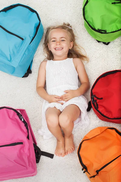Szczęśliwa dziewczyna przedszkola leżącego wśród kolorowych Plecaki szkolne — Zdjęcie stockowe