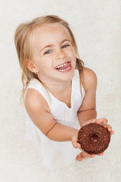 Glückliches kleines Mädchen hält einen mit Schokolade überzogenen Donut in der Hand - — Stockfoto