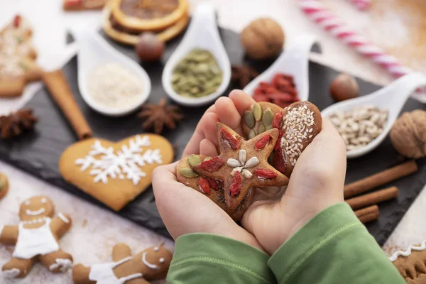 Hands holding gingerbread cookies decorated with natural seeds a — Stock Photo, Image