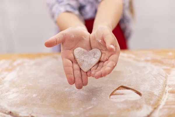 Niña manos con galleta en el sahep de un corazón cortado de t Imágenes de stock libres de derechos