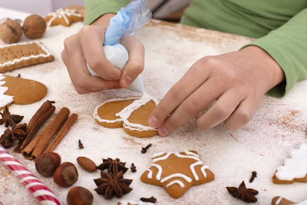 Las manos jóvenes decoran galletas de jengibre con glaseado blanco - clos Imágenes de stock libres de derechos