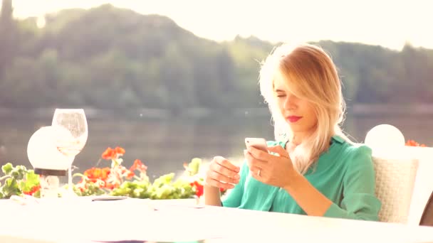 Menina loira encantadora bebe videira e bate-papo com iPhone no restaurante — Vídeo de Stock