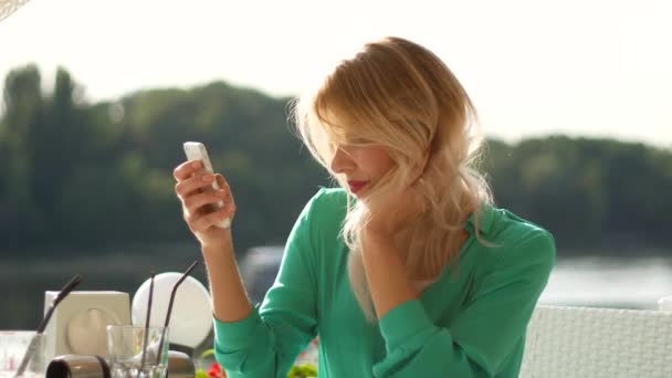 Sorridente ragazza bionda con iPhone in caffè — Video Stock