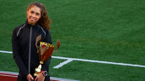 Счастливые улыбающиеся молодые женщины с золотым кубком победы награды на футбольном поле фоне — стоковое видео