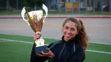 Genç olumlu gülümseyen kız elinde altın kazanan Kupası futbol sahasında tutar.