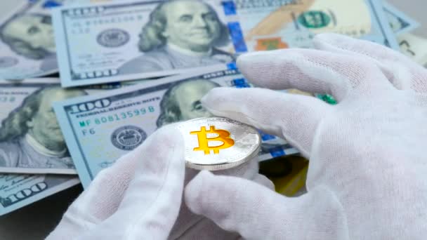 Руками у білих рукавичках оглядають срібний bitcoin cryptocurrency на тлі доларів Usd — стокове відео