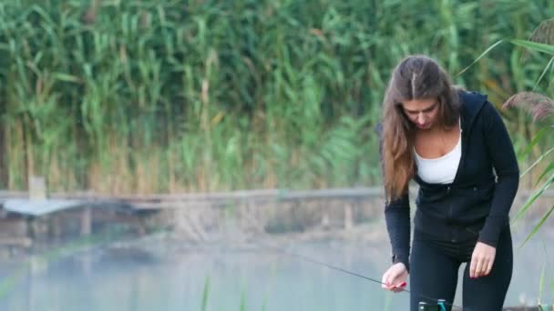 Młoda dziewczyna z zielonym tle trawy wody przygotowuje wędkę przed rozpoczęciem połowów — Wideo stockowe