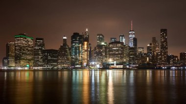 Manhattan şehir merkezinin ünlü gökdelenlerinin gece manzarası. Işıkları suya yansıyan birçok gökdeleni var..