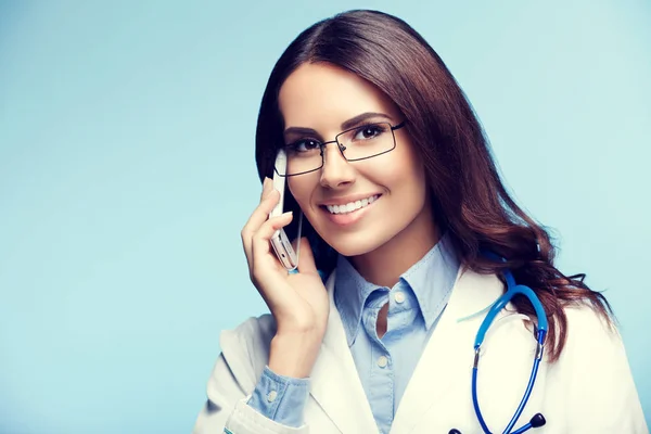 Jeune médecin souriant avec téléphone portable, sur bleu — Photo