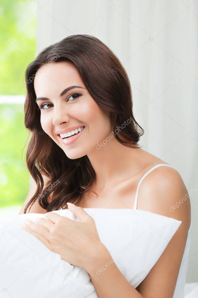 Young beautiful smiling woman waking up with pillow, at bedroom