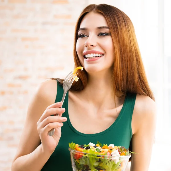 Krásná mladá žena jíst salát, vnitřní — Stock fotografie