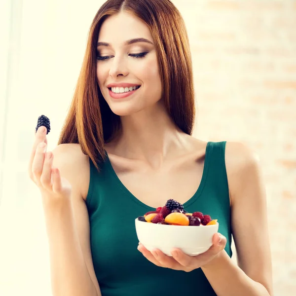 Усміхнена жінка з тарілкою фруктів, в приміщенні — стокове фото