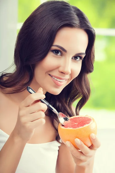 微笑的年轻女子，在家里吃葡萄柚 — 图库照片