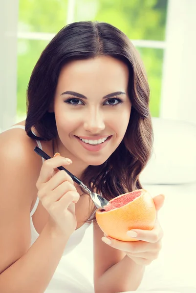 Smiling young woman eating grapefruit at home — Stock Photo, Image